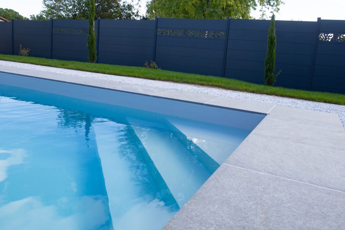 Piscine extérieure avec escalier d'angle, liner gris et margelles grès cérame, volet hors-sol