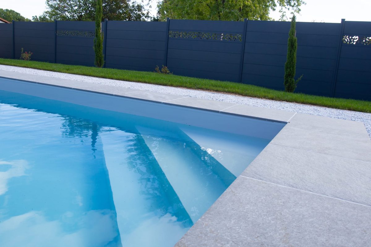 Piscine extérieure avec escalier d'angle, liner gris et margelles grès cérame, volet hors-sol